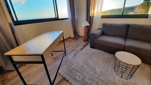 Un salon moderne avec une table en bois, un canapé gris et une table basse ronde dont le piétement est constitué d’une structure en fil de fer.