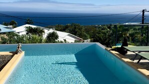 Une piscine d’un bleu éclatant, dotée de chaises longues, entourée de verdure et offrant une vue imprenable sur l’océan.