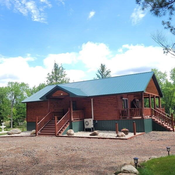 A wooden cabin with a covered porch, a staircase, and a gravel driveway. - Riverfront Bear Cabin (Paris)