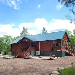 A wooden cabin with a covered porch, a staircase, and a gravel driveway.
