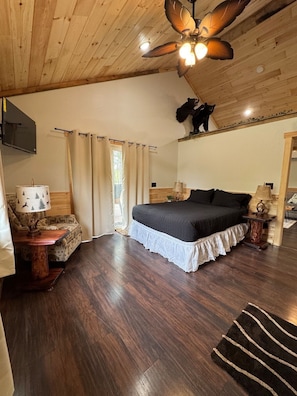 A bedroom with a bed, a ceiling fan, a mounted TV, and a bear decoration on the wall.