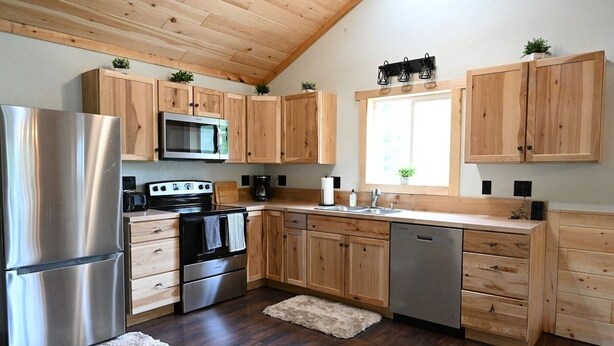 A modern kitchen with wooden cabinets, stainless steel appliances, and a window providing natural light. - Riverfront Bear Cabin (Paris)