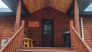 A wooden cabin with a porch, a door, and a sign that reads 'Welcome to the Bear Den.' - Riverfront Bear Cabin (Paris)