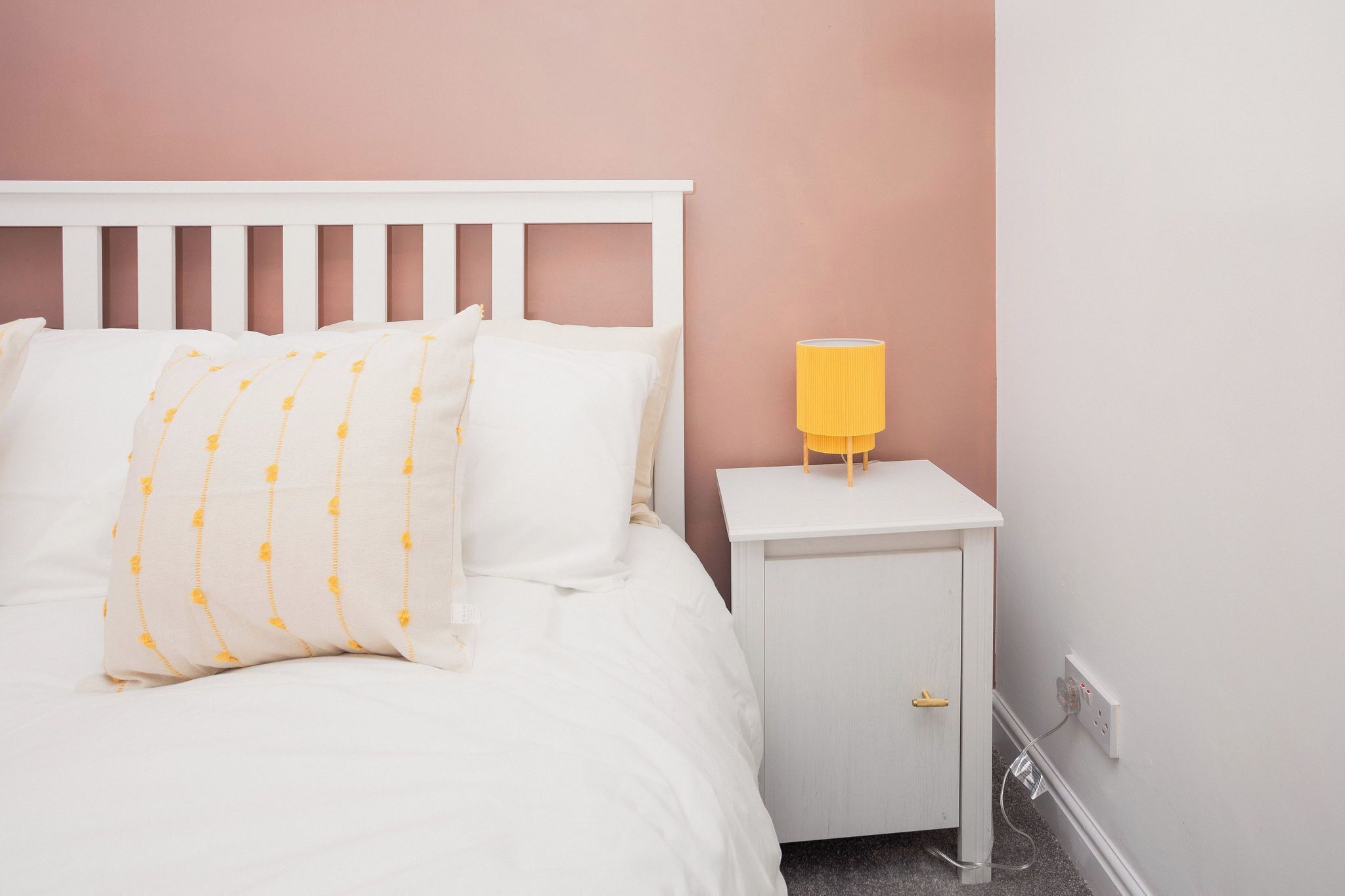 Un lit bien fait, avec du linge de lit blanc et une lampe jaune posée sur une table de chevet.