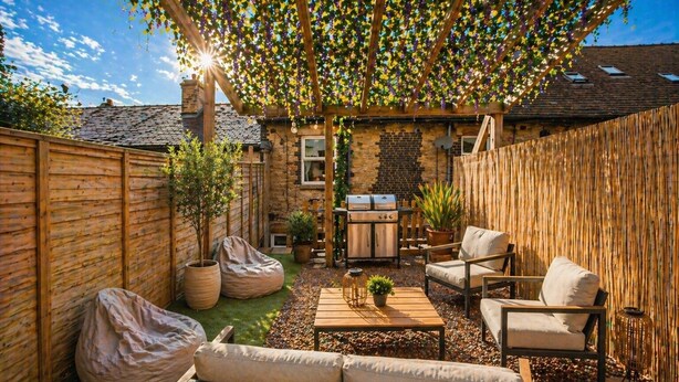 A backyard with a wooden fence, a stone wall, a grill, outdoor seating, and a pergola with hanging plants.