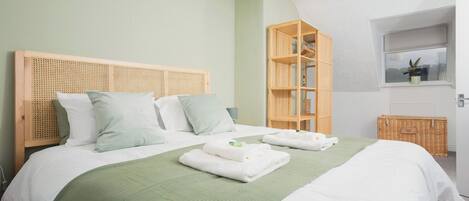 A neatly made bed with a green throw, a wooden headboard, and a wicker basket by the window.