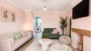 A living room with a sofa, a green couch, a round coffee table, a bean bag, and a TV mounted on the wall.