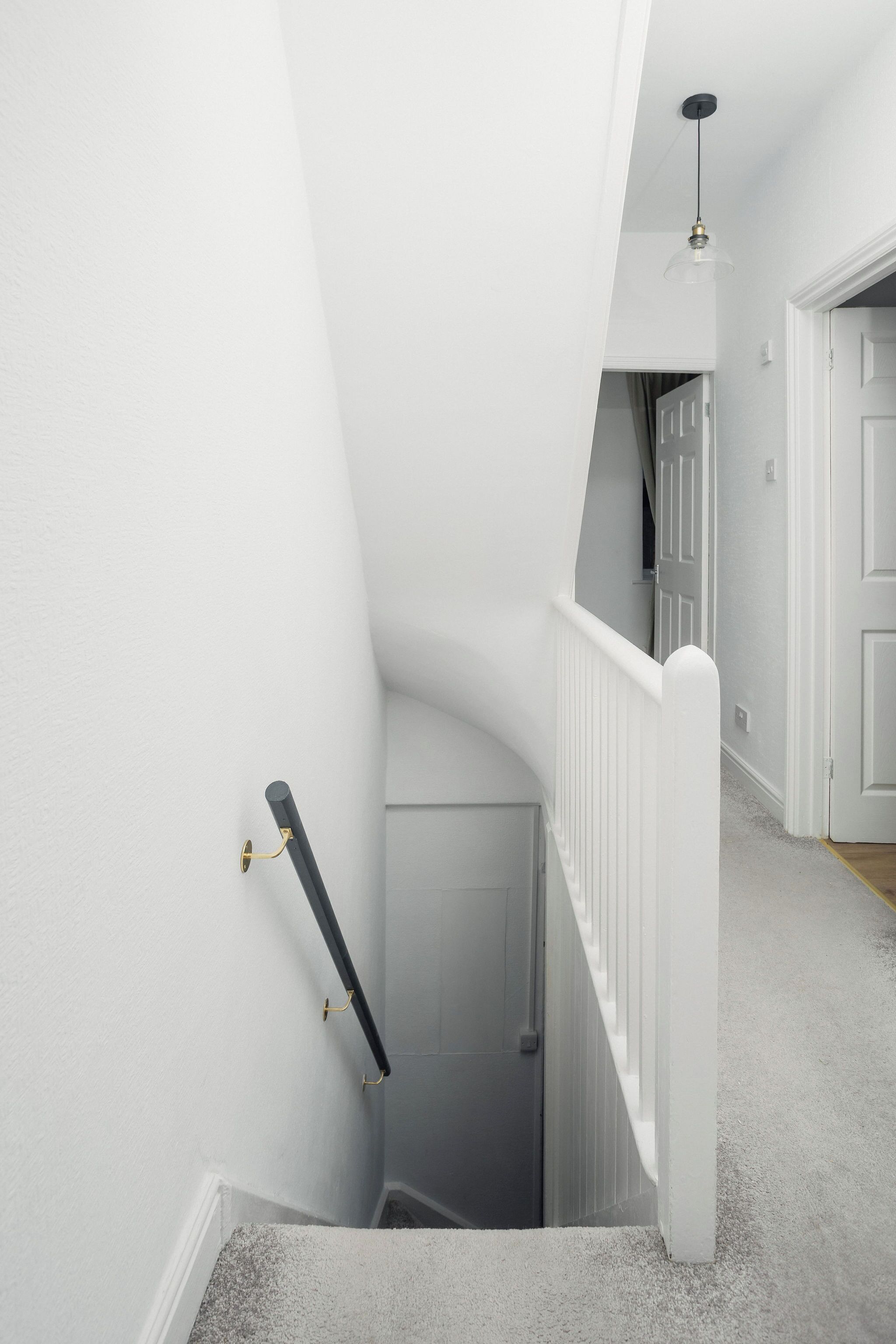 A narrow staircase with a white railing and a black handrail, leading to a door at the top.