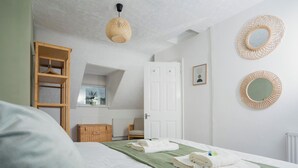 A bedroom with a bed, a wooden wardrobe, a hanging light, and two woven wall decorations.