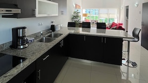 Una cocina moderna con armarios oscuros, encimera de granito y horno integrado. Hay una zona de comedor con un sofá rojo y una planta.