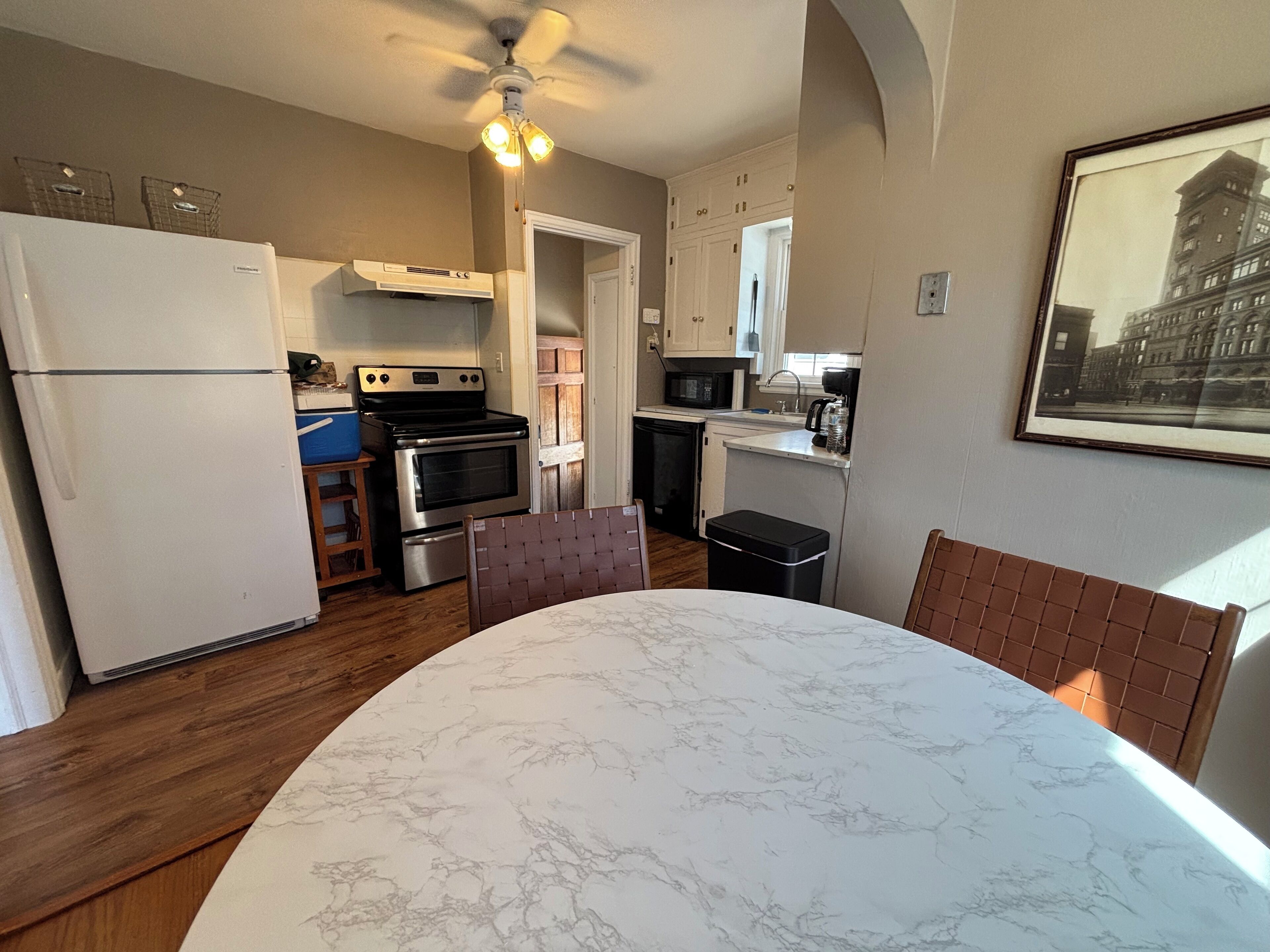 A compact kitchen with a refrigerator, stove, microwave, and sink. There's a dining table with a marble top and two chairs.