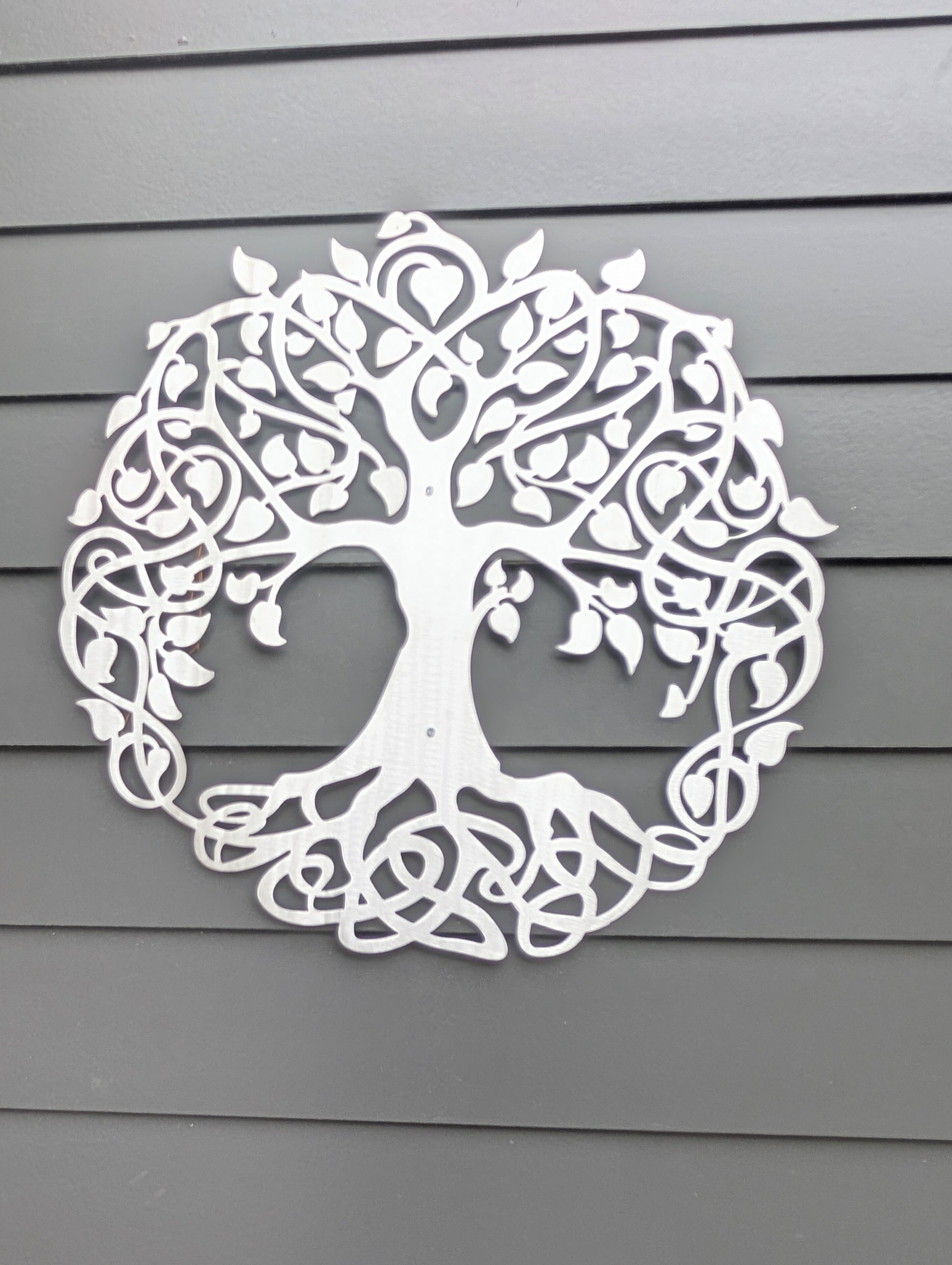 A white, intricate tree-shaped wall decor against a grey wall.