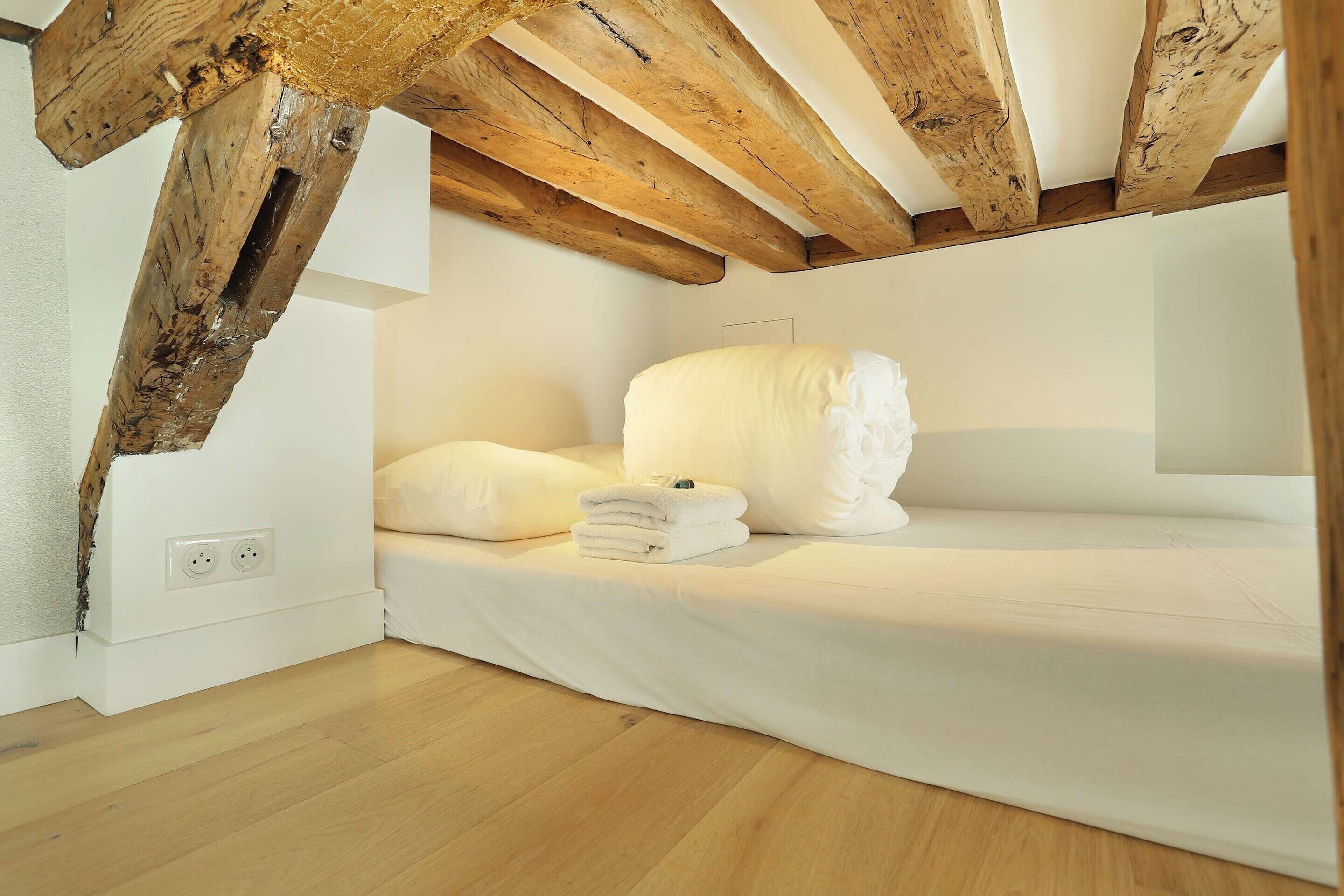 A bedroom with a wooden ceiling, a white bed, and a small bedside table with a lamp.