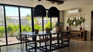 A spacious dining area with a large table and chairs, large windows with a view of greenery, and an air conditioning unit on the wall. - “Elegant 3-Bedroom Apartment with Stunning Views in Cancun (Cancun)