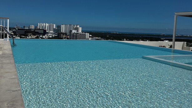 A clear blue pool with a cityscape in the background. - “Elegant 3-Bedroom Apartment with Stunning Views in Cancun (Cancun)
