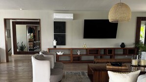 A spacious living room with a large sofa, armchairs, and a coffee table. A flat-screen TV is mounted on the wall, and there is a large mirror above the seating area. - “Elegant 3-Bedroom Apartment with Stunning Views in Cancun (Cancun)