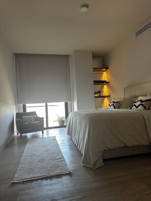 Une chambre avec un grand lit, un canapé, un petit tapis et une fenêtre avec des stores.