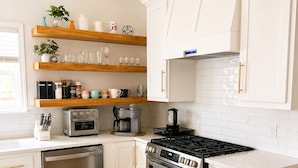 A modern kitchen with white cabinetry, a central island, a built-in oven, a coffee maker, and a dishwasher.