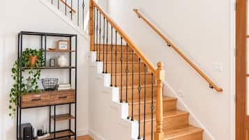 Un escalier avec des marches en bois et des balustrades noires, menant à un palier avec un mur blanc et une petite fenêtre.