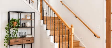 A staircase with wooden steps and black balusters, leading to a landing with a white wall and a small window.