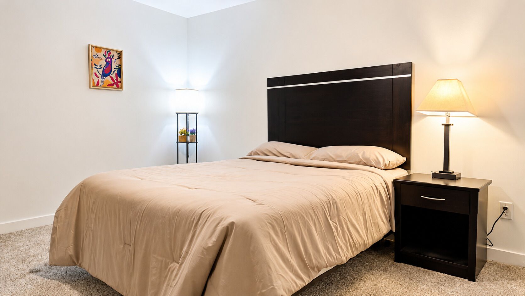 A bedroom with a bed, bedside tables, a lamp, and a wall-mounted artwork.