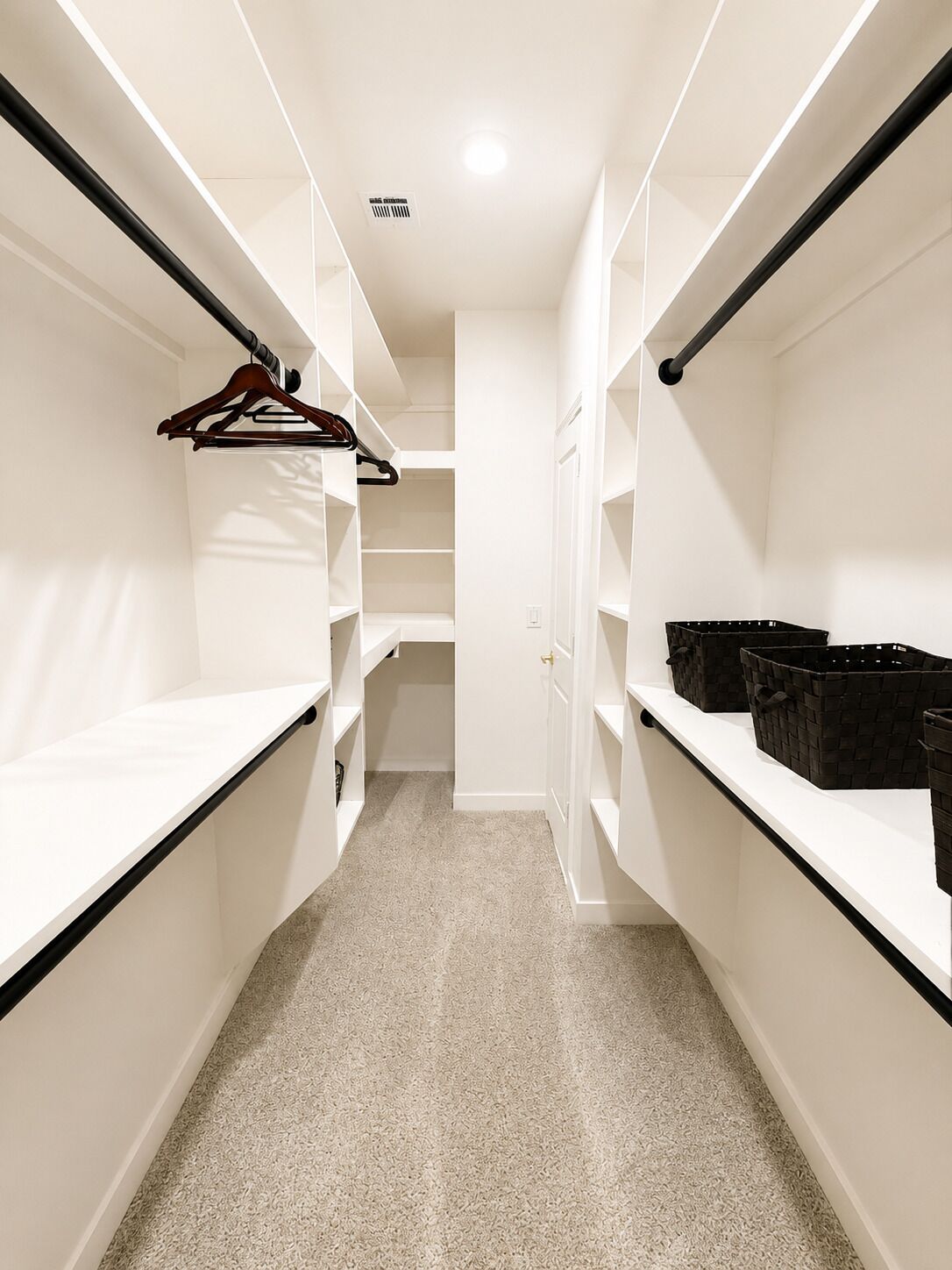 A walk-in closet with white shelving, a hanging rod, and a door leading to another room.