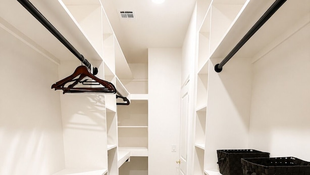 A walk-in closet with white shelving, a hanging rod, and a door leading to another room.