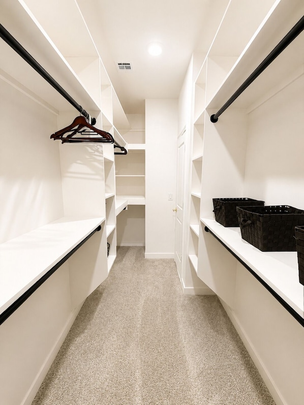 Vestidor con estantes blancos, una barra para colgar ropa y una puerta que da a otra habitación.