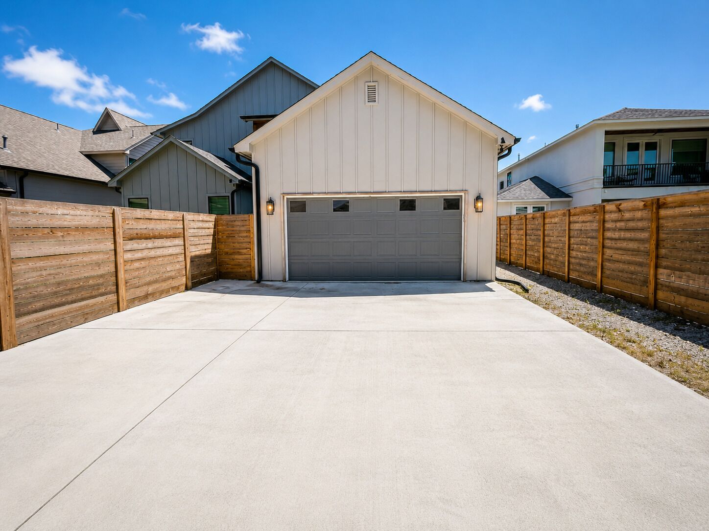 Un garage avec une allée en béton, des clôtures en bois et un luminaire fixé au mur.