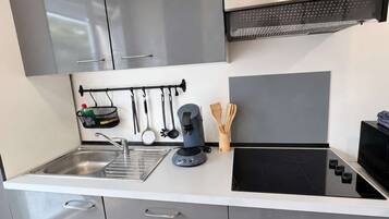 A modern kitchen with grey cabinets, a stainless steel range hood, a built-in oven, and a black stovetop.