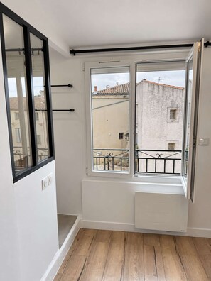 Une pièce dotée d’une grande fenêtre, d’un mur blanc et d’un plancher en bois.