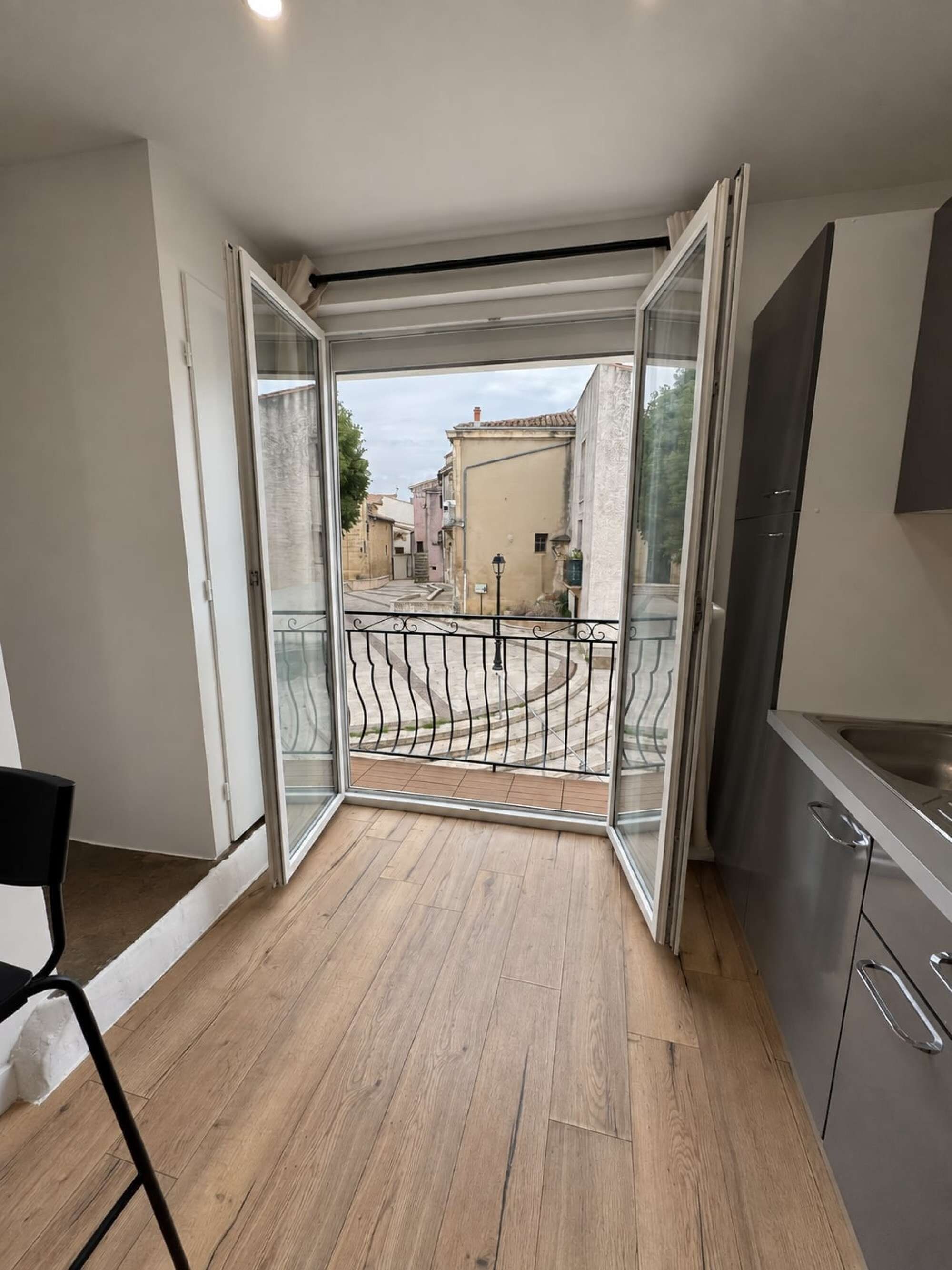 Een open balkon met uitzicht op een straat, een metalen hekwerk en een keuken met kastjes en een spoelbak.