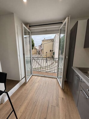 An open balcony with a view of a street, a metal railing, and a kitchen area with cabinets and a sink. - Charming 2-bedroom duplex, tram and free parking (Saint-Jean-de-Védas)