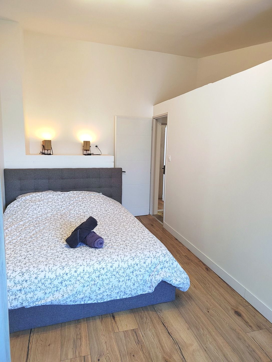 A bedroom with a bed, a headboard, a nightstand, and a wall-mounted light fixture.