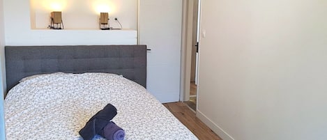 A bedroom with a bed, a headboard, a nightstand, and a wall-mounted light fixture.