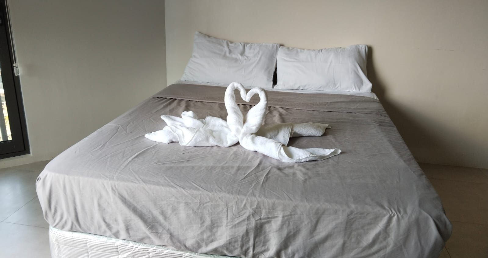 A bed with a grey bedspread and two white towels arranged in a heart shape.