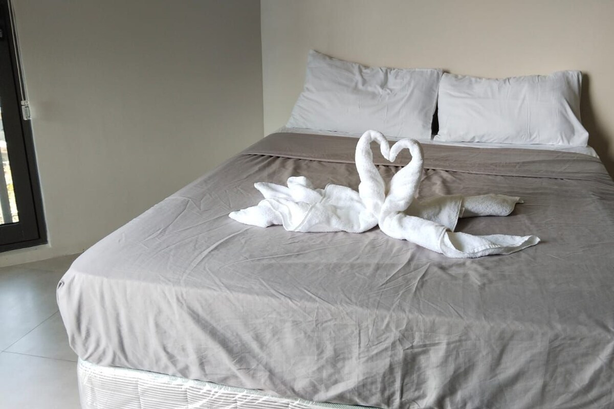 Un lit recouvert d’une couverture grise, avec deux serviettes blanches disposées en forme de cœur.