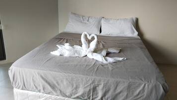 A bed with a grey bedspread and two white towels arranged in a heart shape.