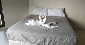 A bed with a grey bedspread and two white towels arranged in a heart shape. - Rent Homecation (Lapu-Lapu)