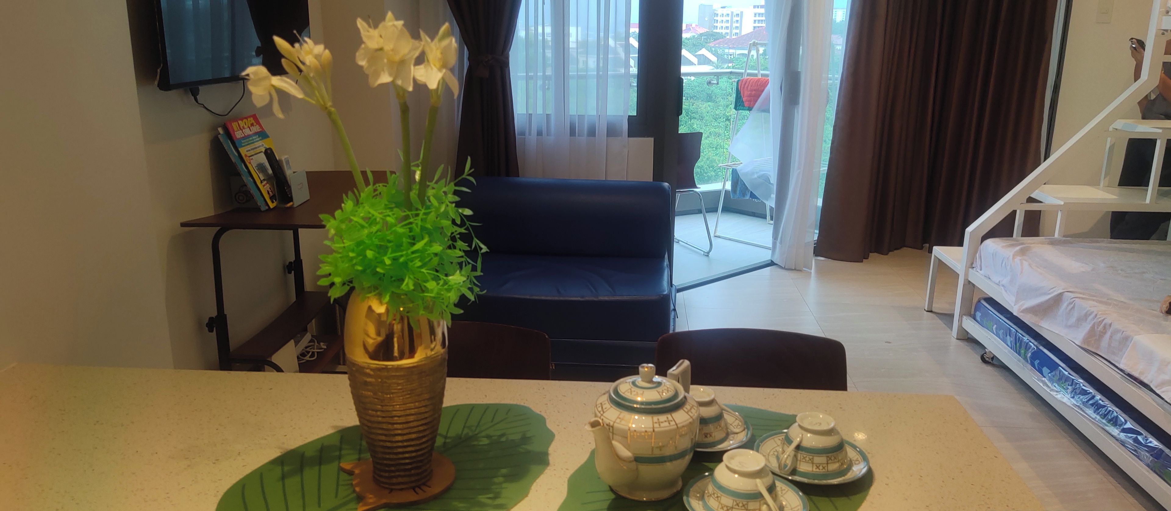 A hotel room with a dining table set with a teapot and cups, a sofa, and a bed.