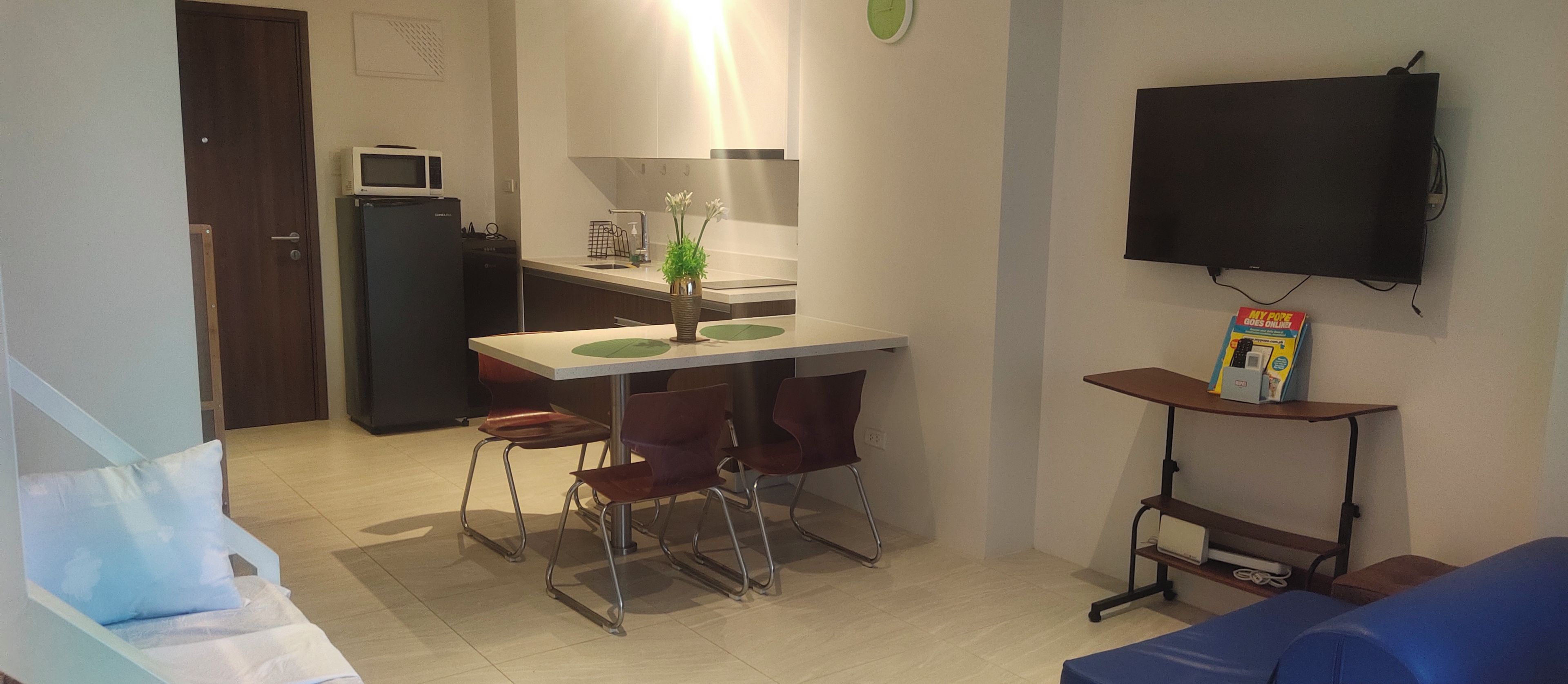 A compact living space with a kitchenette, a dining area, a TV mounted on the wall, and a small seating area.