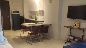 A compact living space with a kitchenette, a dining area, a TV mounted on the wall, and a small seating area.