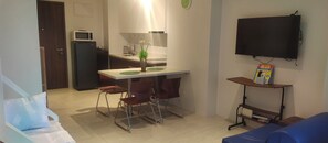 Un espace de vie compact comprenant un coin cuisine, un coin repas, un téléviseur fixé au mur et un petit coin salon.