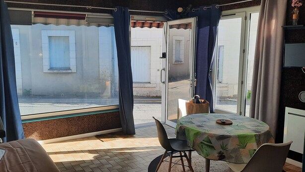 Una habitación con una mesa, sillas, una ventana con cortinas y vista a la calle.