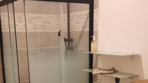 Una ducha con cerramiento de vidrio, un perchero, una pared decorativa con diseños circulares y un inodoro con motivos florales.