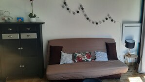 Un dormitorio con cama, cómoda, planta en maceta, aire acondicionado instalado en la pared y ventana con cortinas.