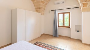 Un dormitorio con cama, armario, ventana con cortinas y suelo de baldosas.