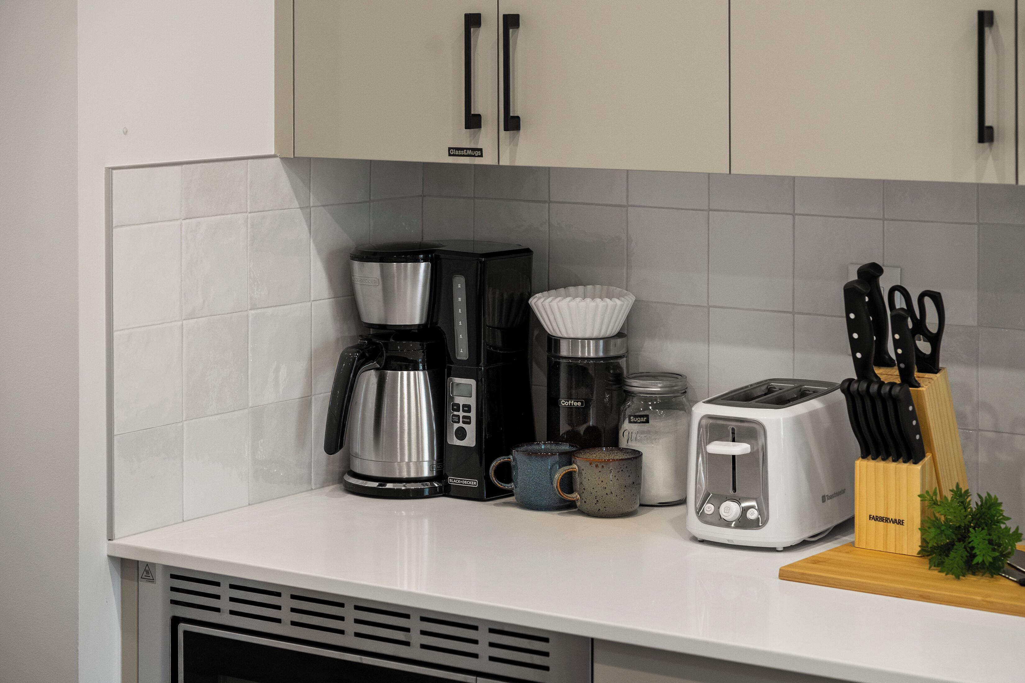 A kitchen counter with a coffee maker, a toaster, a sugar jar, and a knife block.