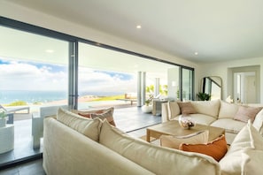 A spacious living area with a large window overlooking a beach, a comfortable sofa set, and a coffee table.