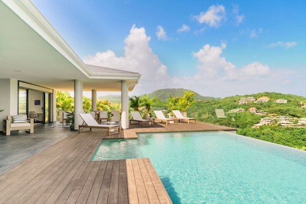 A poolside area with lounge chairs, a wooden deck, and a view of a hillside.